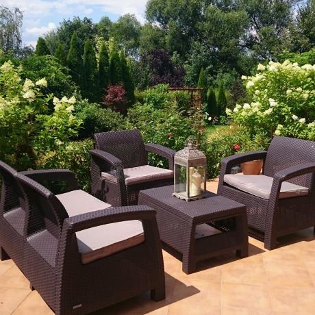 Brązowe meble ogrodowe Allibert Keter Corfu Set w pełnym zieleni ogrodzie