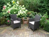 Plastikowe fotele ogrodowe Rattan Style Iowa w otoczeniu ogrodowej zieleni